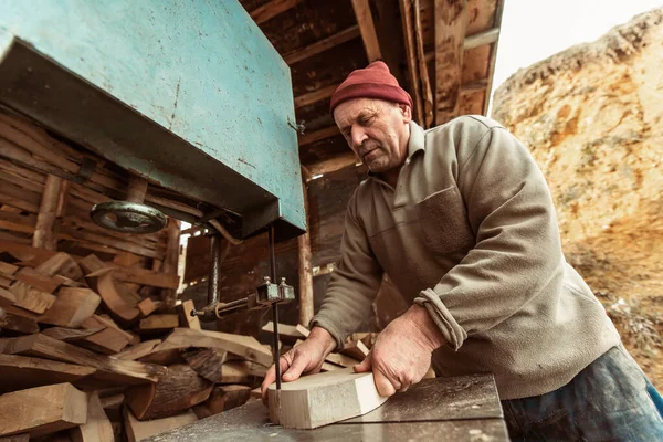 A senior man processing wood on a machine in an outdoor workshop.