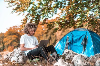 A student with an afro hairstyle sitting in nature and using a laptop.