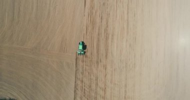 Drone aerial shot of a farmer in tractor seeding, sowing agricultural crops at field.