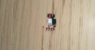 Drone aerial shot of a farmer in tractor seeding, sowing agricultural crops at field.