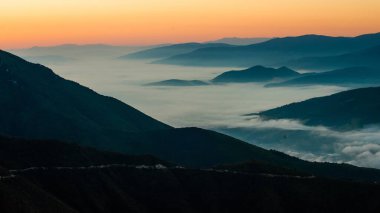 Görünür siluetleri olan dağ siluetleri sabah renkli sislerin arasında.