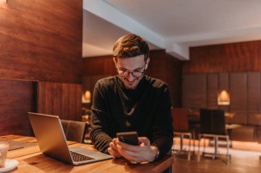 Happy young businessman working on a laptop and smartphone in a cafe. 