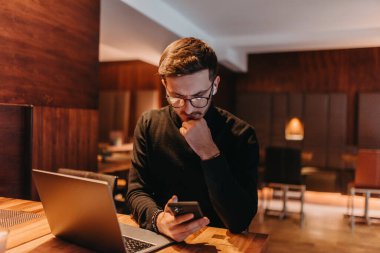 Happy young businessman working on a laptop and smartphone in a cafe. 