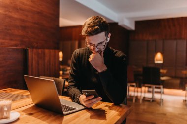 Happy young businessman working on a laptop and smartphone in a cafe. 