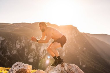 Man doing conditioning training on top of a mountain in the early morning with the sunrise in the background.