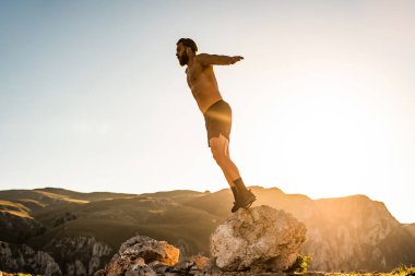 Man doing conditioning training on top of a mountain in the early morning with the sunrise in the background.