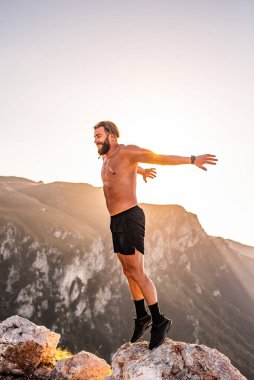 Man doing conditioning training on top of a mountain in the early morning with the sunrise in the background.