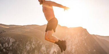 Man doing conditioning training on top of a mountain in the early morning with the sunrise in the background.