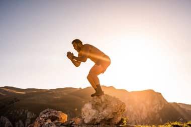 Man doing conditioning training on top of a mountain in the early morning with the sunrise in the background.