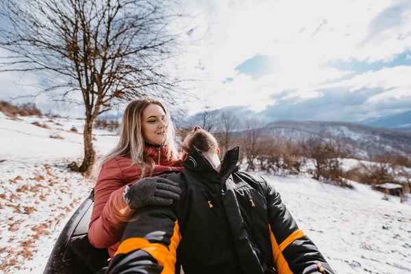 Couple enjoying while driving quad bike on top of mountain at winter time.