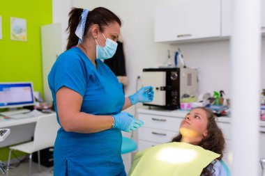 Dişçi hastayla konuşuyor. Dikkatlice dinleyen küçük bir kıza tavsiye veren bir dişçi.. 