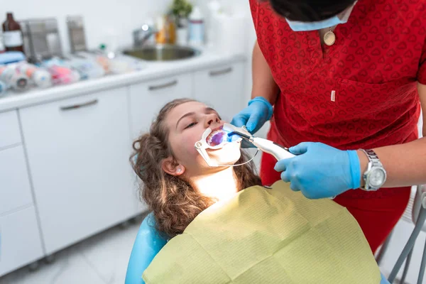 The dentist uses an ultraviolet lamp while fitting the girl with braces.