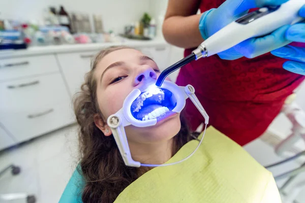 The dentist uses an ultraviolet lamp while fitting the girl with braces.