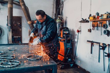 Özel kıyafet ve gözlüklü bir çilingir üretim işinde çalışıyor. Açı öğütücüyle metal işleme. Metal işçiliğinde kıvılcımlar