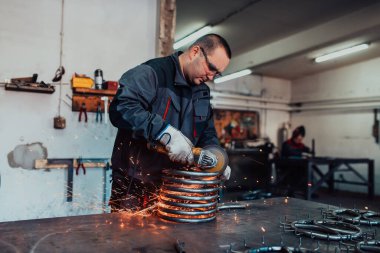 Özel kıyafet ve gözlüklü bir çilingir üretim işinde çalışıyor. Açı öğütücüyle metal işleme. Metal işçiliğinde kıvılcımlar