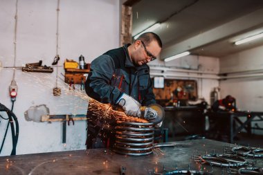 Özel kıyafet ve gözlüklü bir çilingir üretim işinde çalışıyor. Açı öğütücüyle metal işleme. Metal işçiliğinde kıvılcımlar