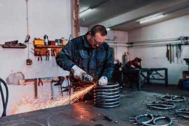 Özel kıyafet ve gözlüklü bir çilingir üretim işinde çalışıyor. Açı öğütücüyle metal işleme. Metal işçiliğinde kıvılcımlar