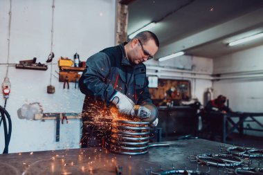 Özel kıyafet ve gözlüklü bir çilingir üretim işinde çalışıyor. Açı öğütücüyle metal işleme. Metal işçiliğinde kıvılcımlar