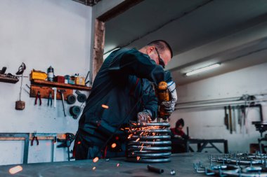 Özel kıyafet ve gözlüklü bir çilingir üretim işinde çalışıyor. Açı öğütücüyle metal işleme. Metal işçiliğinde kıvılcımlar