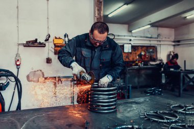 Özel kıyafet ve gözlüklü bir çilingir üretim işinde çalışıyor. Açı öğütücüyle metal işleme. Metal işçiliğinde kıvılcımlar