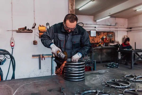 Özel kıyafet ve gözlüklü bir çilingir üretim işinde çalışıyor. Açı öğütücüyle metal işleme. Metal işçiliğinde kıvılcımlar