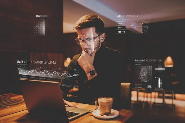 Biometric security, the hologram of online security. Biometric security of eye, voice, finger and face. A man using a laptop in a cafe