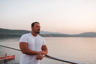 Kumlu bir sahil yakınındaki bir otelde tatil yapan fit ve çekici bir adam. O şık bir şapka takıyor ve sıcak güneşin ve kristal berrak denizin tadını çıkarıyor. Manzara huzurlu ve huzurlu, bir duyguyu yansıtıyor.