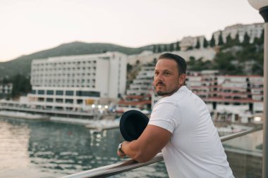 Kumlu bir sahil yakınındaki bir otelde tatil yapan fit ve çekici bir adam. O şık bir şapka takıyor ve sıcak güneşin ve kristal berrak denizin tadını çıkarıyor. Manzara huzurlu ve huzurlu, bir duyguyu yansıtıyor.