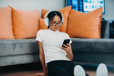 Bir kadın video görüşmesi için kulaklıkları ve akıllı telefonuyla evde egzersiz yapıyor. Modern yaşam tarzını, harmanlama teknolojisini, sağlığını ve bütünsel refahı yansıtır.. 