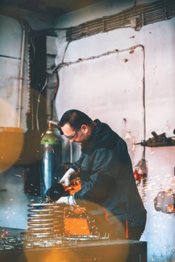 Özel kıyafet ve gözlüklü bir çilingir üretim işinde çalışıyor. Açı öğütücüyle metal işleme. Metal işçiliğinde kıvılcımlar