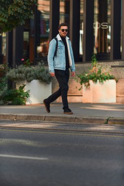 Öğrenci şehirde güneş gözlüğü takıyor, sırt çantası taşıyor, kablosuz kulaklık takıyor, modern şehir yaşam tarzını somutlaştırıyor ve hareket halindeyken bağlı kalabiliyor.