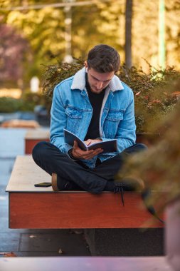 Şehir merkezinde bir bankta oturup kablosuz kulaklık takmış kitap okuyan edebiyatın gücünü ve yoğun bir ortamda dikkat dağıtıcı şeyleri görmezden gelme yeteneğini gösteren bir adam.