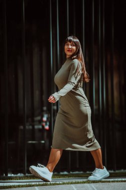 Kendine güvenen ve tarz sahibi bir kadın zeytin yeşili bir elbiseyle modern bir binanın önünden geçiyor. Işıl ışıl bir güzellik, güç ve kendini beğenmişlik.