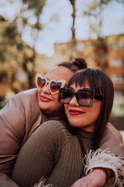 2人の若い女性がサングラスをかけながら晴れた日に感情的に外にお互いを受け入れる — ストック写真