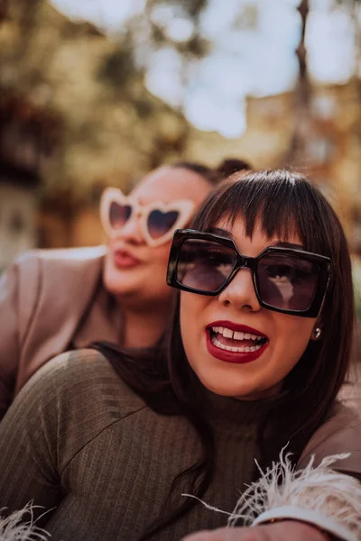 2人の若い女性がサングラスをかけながら晴れた日に感情的に外にお互いを受け入れる — ストック写真