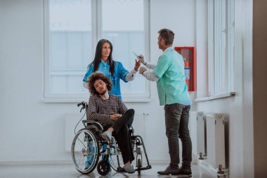 Doktor ve hemşire hastaların sağlığını tartışırken tekerlekli sandalyedeki hasta onların yanında.