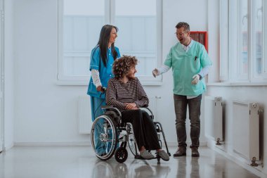Doktor ve hemşire hastaların sağlığını tartışırken tekerlekli sandalyedeki hasta onların yanında.