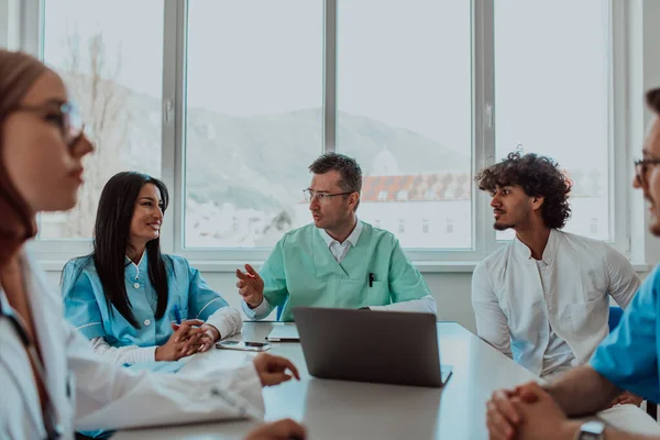 stock image A group of multiethnic medical professionals including doctors, surgeons, and nurses are gathered in a hospital setting discussing patient care and using modern technology to address challenges in