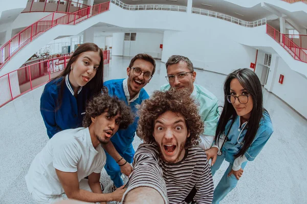 Modern bir hastane koridorunda, bir doktor ve bir tıp hemşiresi tekerlekli sandalyedeki bir hastayla selfie çekiyor, neşe saçıyor, kapsayıcılık ve teknolojinin sağlık hizmetleri üzerindeki olumlu etkisi