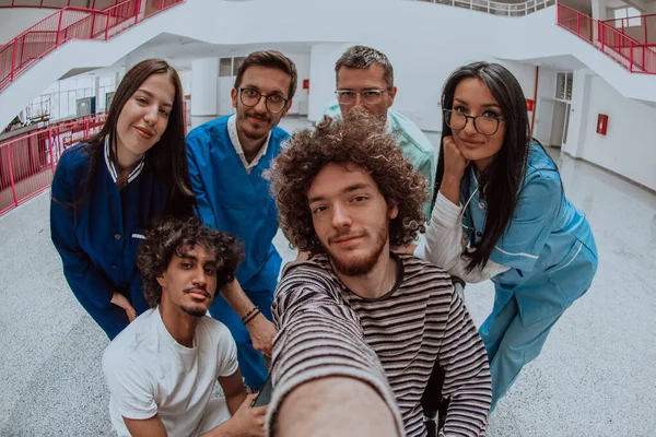 Modern bir hastane koridorunda, bir doktor ve bir tıp hemşiresi tekerlekli sandalyedeki bir hastayla selfie çekiyor, neşe saçıyor, kapsayıcılık ve teknolojinin sağlık hizmetleri üzerindeki olumlu etkisi