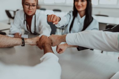 Bir grup doktor ve bir tıp hemşiresi bir masada el ele tutuşarak, sağlık alanındaki ortak çabalarını yönlendiren sarsılmaz takım çalışmasını ve dayanışmayı sergilediler..