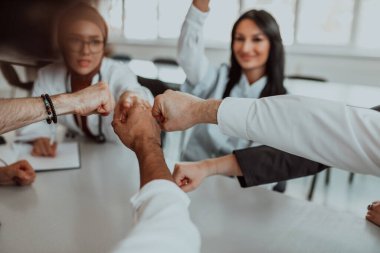 Bir grup doktor ve bir tıp hemşiresi bir masada el ele tutuşarak, sağlık alanındaki ortak çabalarını yönlendiren sarsılmaz takım çalışmasını ve dayanışmayı sergilediler..