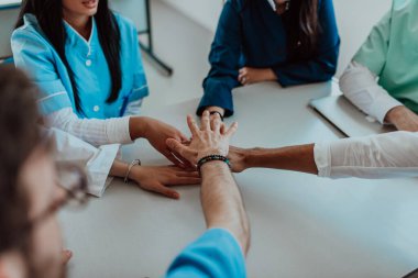 Bir grup doktor ve bir tıp hemşiresi bir masada el ele tutuşarak, sağlık alanındaki ortak çabalarını yönlendiren sarsılmaz takım çalışmasını ve dayanışmayı sergilediler..