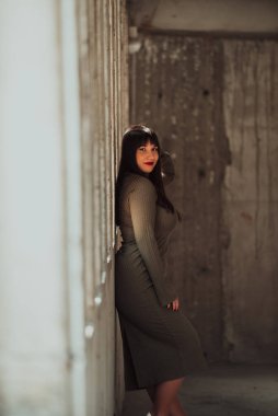 Zeytin yeşili bir elbiseyle modern bir bina tarafından poz veren kendine güvenen ve şık bir kadın. Işıldayan güzellik, güç ve kendini beğenmişlik.