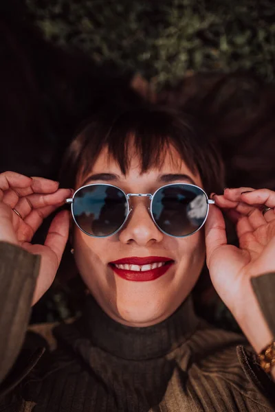 Молода Жінка Сонцезахисними Окулярами Лежить Траві Показуючи Красиве Обличчя Безтурботним — стокове фото