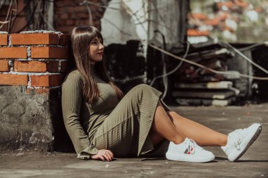 Kendine güvenen ve tarz sahibi bir kadın zeytin yeşili bir elbiseyle modern bir binanın önünden geçiyor. Işıl ışıl bir güzellik, güç ve kendini beğenmişlik.