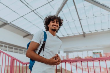 Mavi sırt çantalı Afro-Amerikan bir öğrenci, modern Afro saç stili ve geniş bir gülümseme ile, coşku yayıyor ve modern bir üniversitenin coşkulu ruhunu temsil ediyor, hırsını somutlaştırıyor.