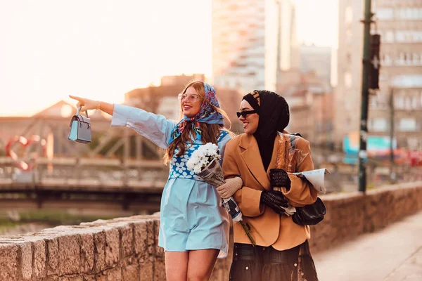 ヒジャーブと現代的で伝統的なドレスを着たカップルの女性と 青いドレスとスカーフを着たカップルは 日没時に街を歩いています 花束とパンを持っているのに対し — ストック写真