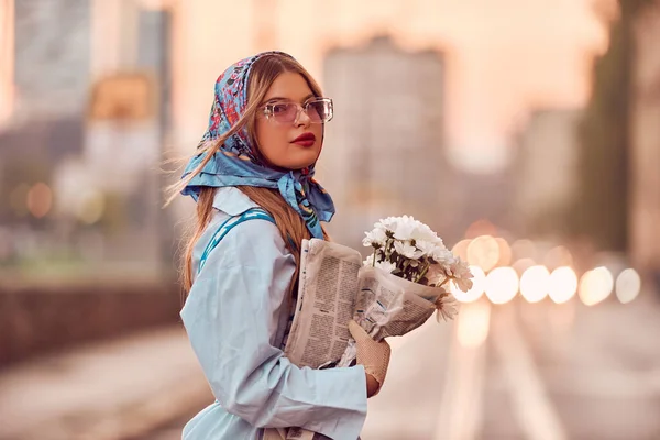 迷人的女人穿着精致的蓝色传统服装 提着蓝色的手提包和一束鲜花 在夕阳西下优雅地在城市里漫步 营造出迷人的景色 — 图库照片