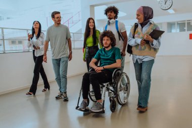 Modern bir üniversitede, aralarında Afro-Amerikalı bir öğrenci ve tesettürlü bir kadının da bulunduğu bir grup öğrenci, tekerlekli sandalyeye mahkum meslektaşlarıyla birlikte koridorda birlikte yürüyorlar.